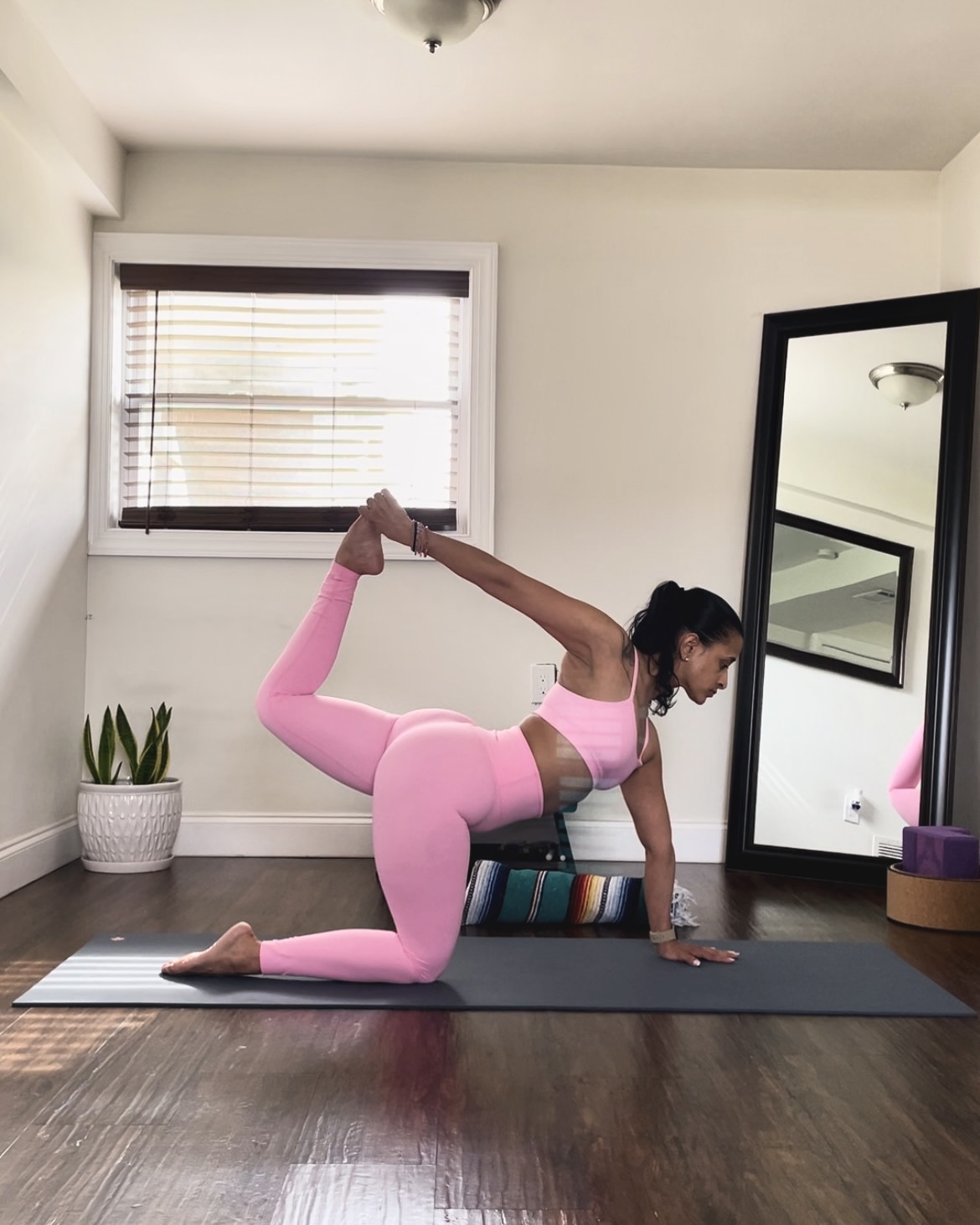 Woman in pink yoga attire practicing a backbend pose on a mat in a bright home studio